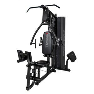 Pilnas jėgos staklių TOORX MSX-90 vaizdas iš priekio. Treniruoklis yra juodos spalvos, su įvairiais priedais ir svarmenų bloku kairėje pusėje.