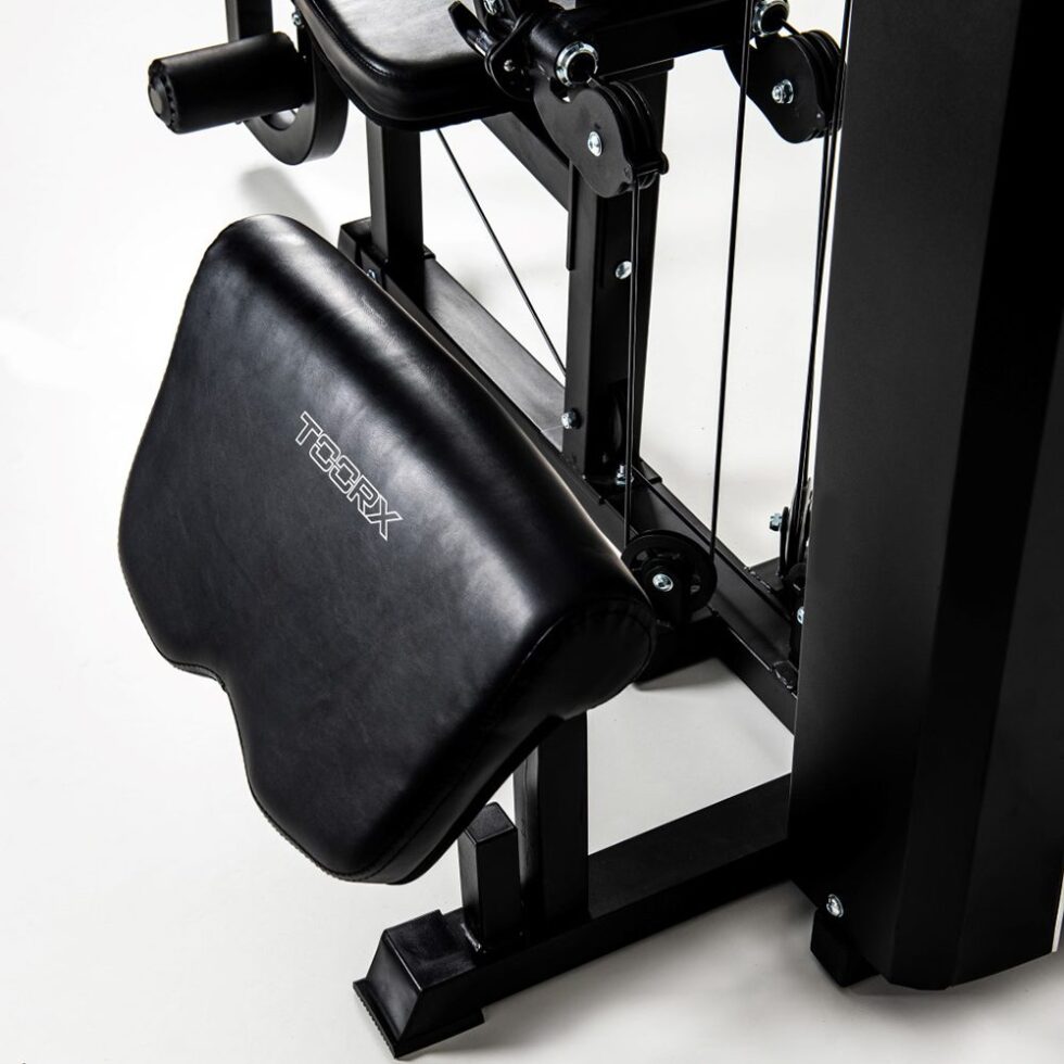 Iš arti nufotografuota TOORX MSX-90 jėgos staklių sėdynės ir kojų atramos dalis su „TOORX“ logotipu, rodanti apmušalų tekstūrą ir mechanizmą